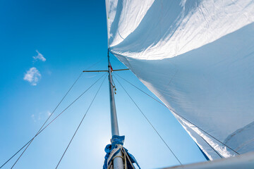 imagen con vista inferior de el mástil de un velero en un día soleado y su vela mayor ondeando por el viento