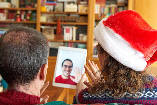 Christmas video call concept. Senior couple with female wearing santa hat waving at son on tablet