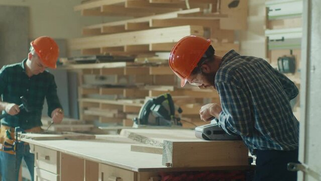 Carpenters Wearing Hard Hat on Head and Protective Glasses Working With a Piece of Furniture and a Lathe in Their Workshop.Woodworking. Manual Labor. Carpentry, Craftsmanship, and Handwork Concept.