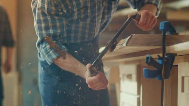 Close-up of a Young Artisan Craftsman in a Checkered Shirt, and Protective Glasses Using a Hand Scraper to Remove the Bark from the Wood Bar. Woodworking. Hands with a Sharp Knife. Wood Knife