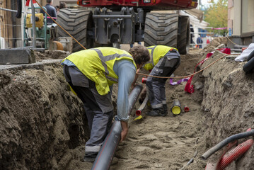 Workers install underground pipes for water, sewerage, electricity and fiber optics for the population of an urban center. - obrazy, fototapety, plakaty