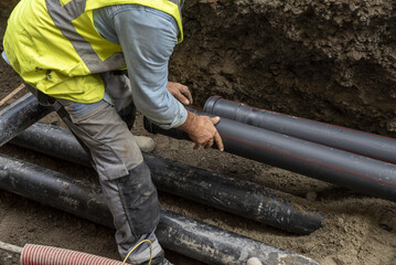Workers install underground pipes for water, sewerage, electricity and fiber optics for the population of an urban center. - obrazy, fototapety, plakaty