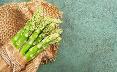 Fresh asparagus bunch on canvas napkin on green table background, top view, space for text