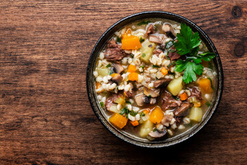 Autumn food. Warming soup with pumpkin, mushrooms, vegetables, beef and barley. Rustic wood table background, top view
