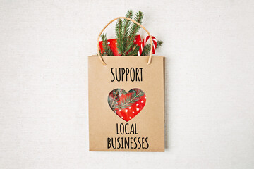 Support Local Business text written on paper shopping bag. Flat lay with Support Local Business quote, Christmas decoration and shopping bag, gift boxes and staff.