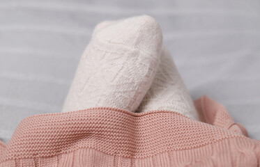 Women's feet in knitted woolen white socks at home under a plaid. Selective focus.