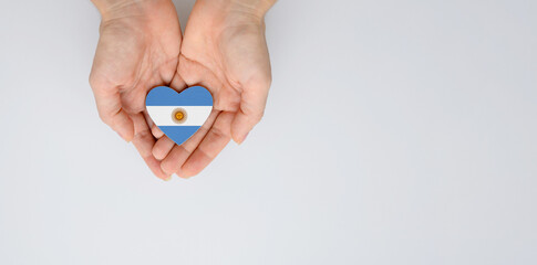 The national flag of Argentina in the shape of a heart in the hands on a light background. Flat...