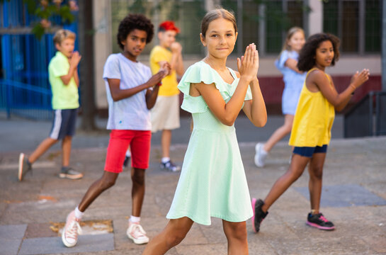 Young positive girl performing dance with her friends during rehearsal outdoors.