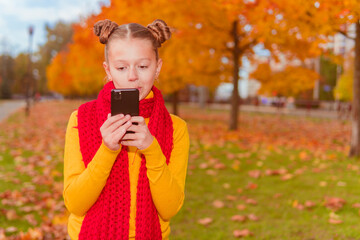 a teenage girl in a red scarf stands with a phone against the background of an autumn park in yellow leaves