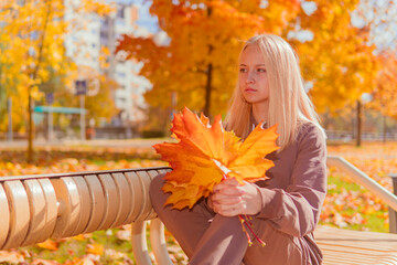 Naklejka na ściany i meble a teenage girl sits on a bench against the background of yellow autumn trees