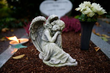 small angel figure with wings on a grave with flowers and burning candle at dusk