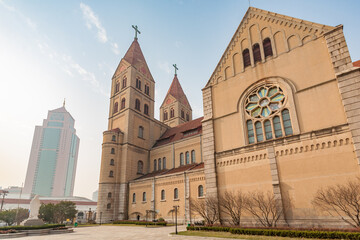 QINGDAO, SHANDONG PROVINCE, CHINA: St. Michael's Cathedral, architectural contrast with massive glass and concrete high rise - obrazy, fototapety, plakaty