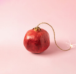 red pomegranate lke bomb with lit fuse on bright pink background. minimal creative composition.