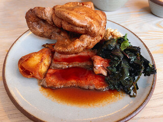 Very large Yorkshire pudding on a plate with sliced roast beef and gravy.