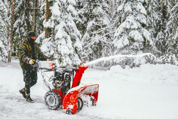 a man cleans the road from snow with a snowplow in the forest in winter against the backdrop of a...