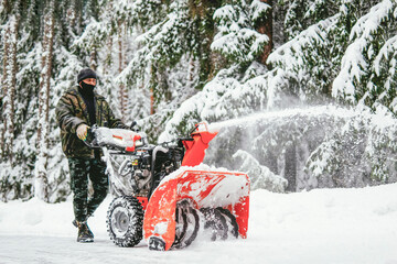 a man cleans the road from snow with a snowplow in the forest in winter against the backdrop of a snowy forest