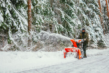 a man cleans the road from snow with a snowplow in the forest in winter against the backdrop of a...