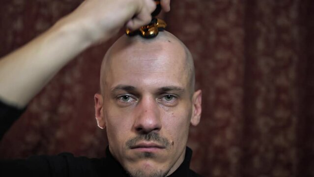 Portrait of a bald man who shaves his head with an electric razor. Close-up a man who has lost his hair takes care of his hair and scalp.