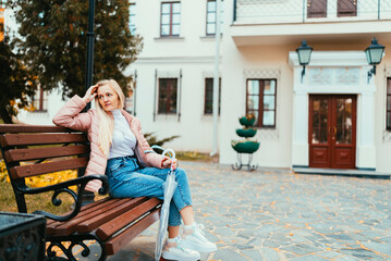 A blonde girl sits on a bench and walks around the city against the backdrop of autumn leaves and laughs on a sunny day