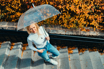 A blonde girl with an umbrella walks around the city against the background of autumn leaves on an...