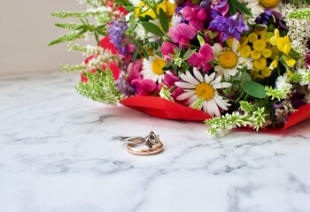 Wedding ring on a white table on the background of a bouquet of flowers. Gold and silver ring. Wedding concept