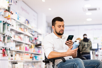 Male customer in wheelchair scans the barcode on a medicine bottle with his smartphone