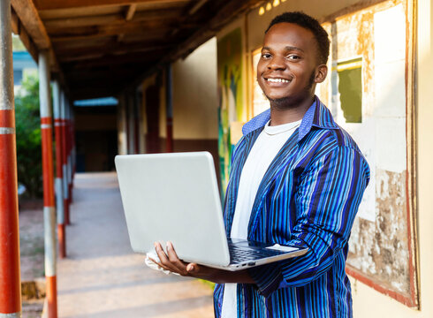 Attractive young african male student standing in a vivid school environment holding laptop device