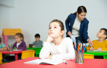 Portrait of tired schoolgirl sitting at pupils desk at lesson in primary school