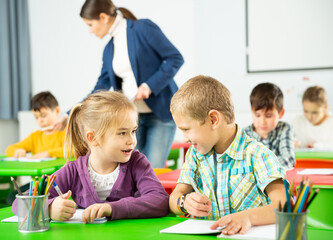 Portrait of happy schoolchildren sitting in classroom and chatting during lesson
