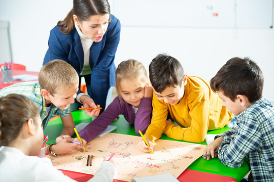 Pretty boys and girls with teacher draw a table game in classroom. High quality photo
