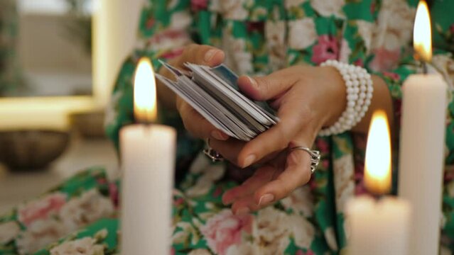 Crystal watcher hands shuffling tarot cards by candlelight. Fortune teller ritual for predicting the future