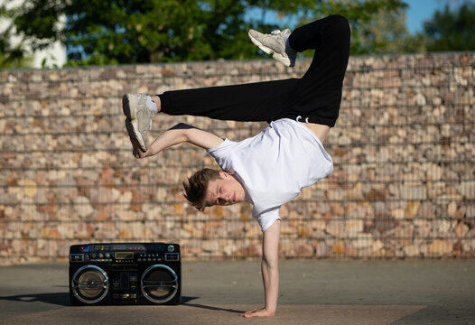 A boy in a breakdance position. Dancer in a difficult breakdance position. A young boy in a white T-shirt and black pants is dancing breakdance. The teenager is dancing at the boombox.