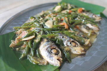 Green chili fish in aluminum tray lined with banana leaves on wooden table

