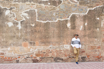 Hombre con sombrero, recargado en una pared de hacienda abandonada posando