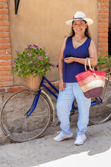 Latina morena con sombrero en la calle, bolsa en mano y al lado de una bicicleta