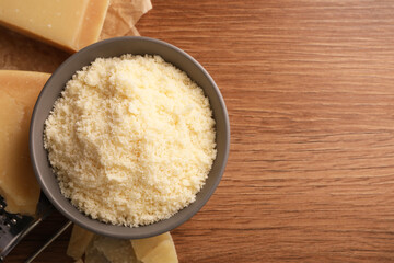 Delicious grated parmesan cheese in bowl on wooden table, flat lay. Space for text