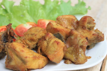 Fried chicken on a white plate with lettuce and tomato slices on a wooden table