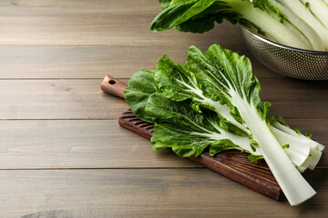Leaves of fresh green pak choy cabbage with water drops on wooden table, space for text