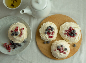 Mini pavlova meringue cakes with red and black currants. Serving on a round board. View from above