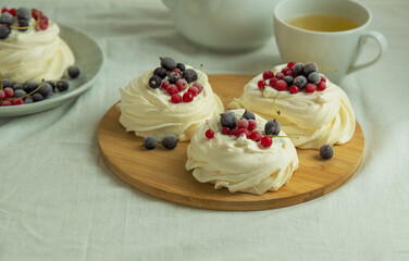 Mini pavlova meringue cakes with red and black currants. Serving on a round board. Side view