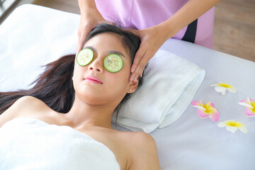 Young beautiful  asian woman relaxing with face massage at beauty spa salon. using cucumber holding around her eyes.