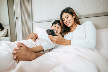 Young Asian couple enjoy with mobile phone in bedroom