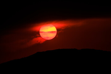 Close-up. Picturesque sunset in cloudy weather. The red sun sets over the horizon. The setting sun is hidden behind storm clouds.