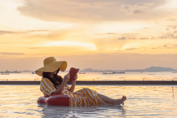 Relaxation , Meditation Concept - Asian young woman with hat covered half face sitting on the inflatable ring, relaxing at pool in a luxurious beachfront hotel at sunset enjoying perfect beach holiday