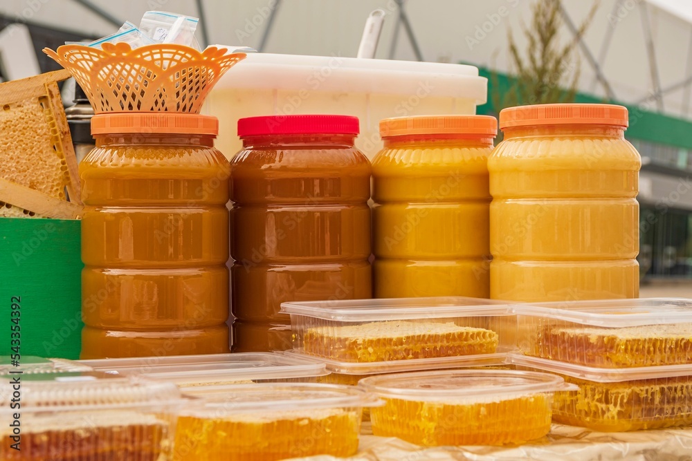 Wall mural Plastic jars filled with multi-colored ripe bee honey. There is trade at autumn agricultural fair.