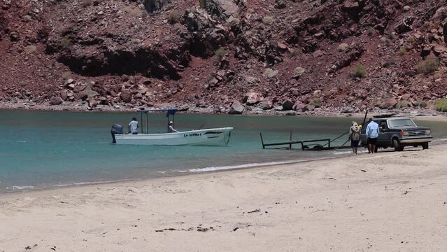 Panga driving up to a boat trailer in the water with a cliff in the background