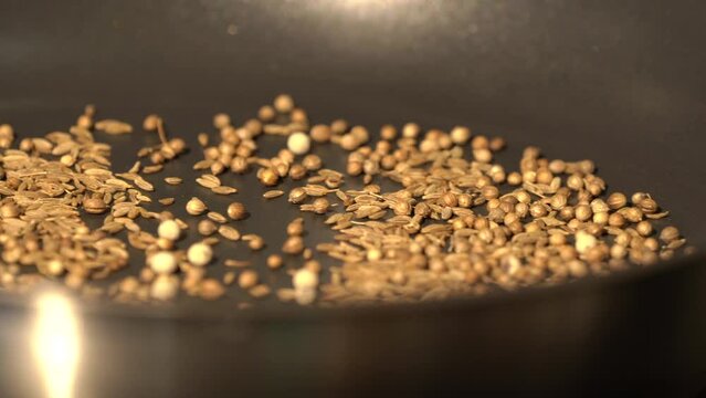 Spices, grains and herb seed are being roasted in pan on an electric stove by Asian man chef. 