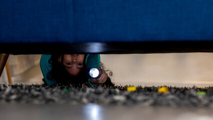 Girl with a flashlight looking under the bed. evening night time. kid girl afraid of monsters hold...