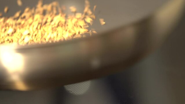 Spices, grains and herb seed are being roasted in pan on an electric stove by Asian man chef. 