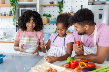 Happy family cooking together on kitchen. Mother and daughter with father cooking. Dad and daughter chopping green vegetable leaf for salad. Home recreation and food preparation on weekend